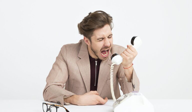 man wearing brown suit jacket mocking on white telephone