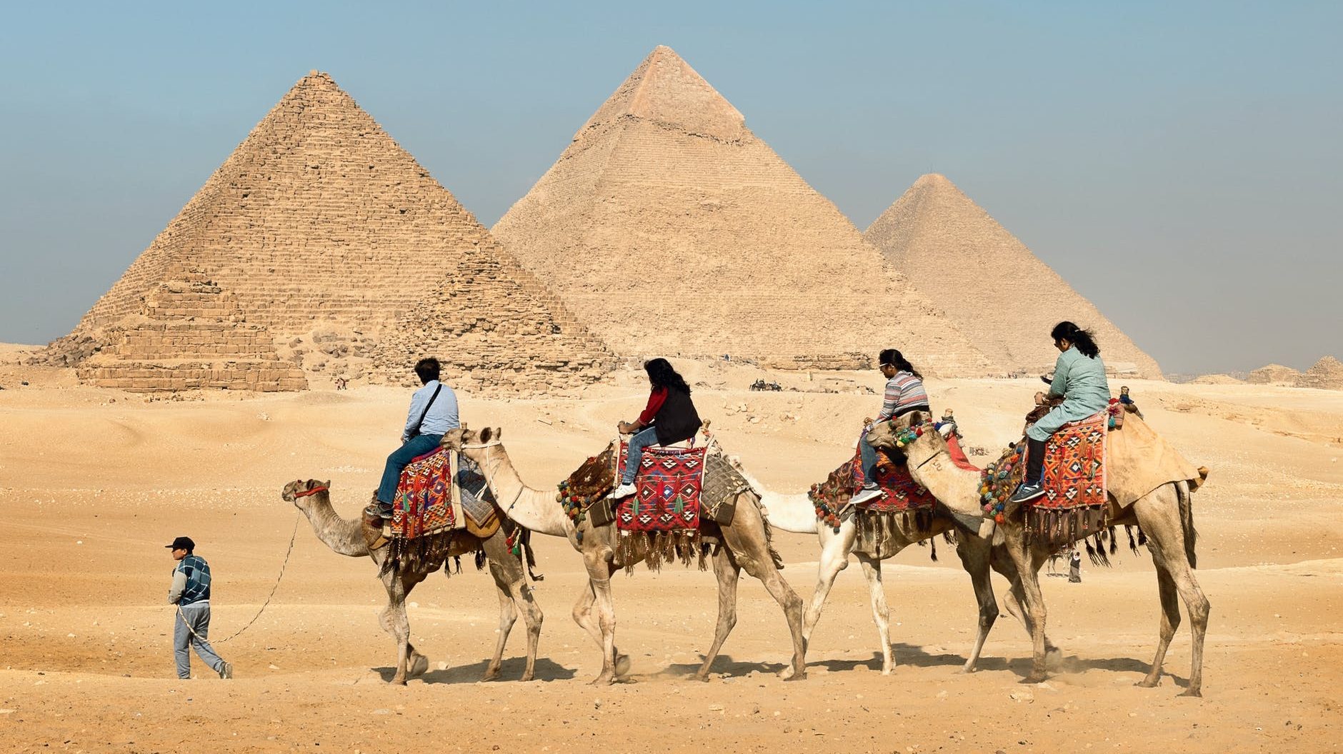 four people riding on camels across the pyramids