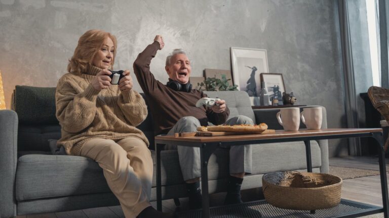 elderly couple sitting on couch playing video games