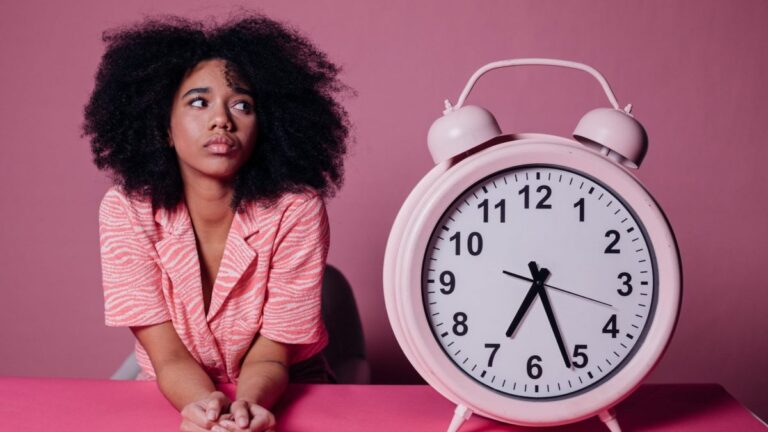 woman in pink long sleeve shirt sitting beside white and pink alarm clock